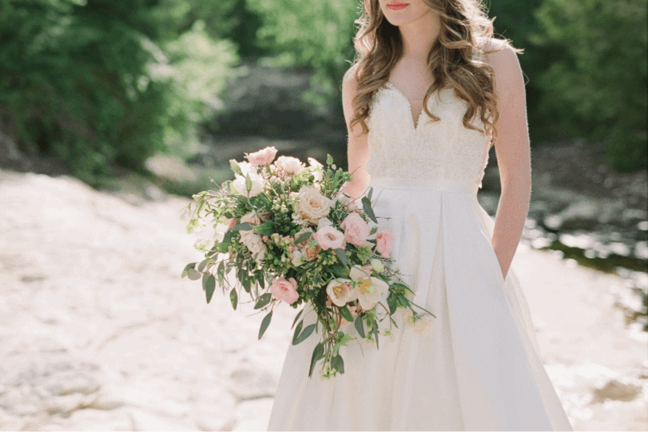 A bride holds a boquet with pink and peach colored flowers