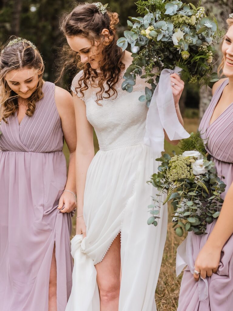 A bride holds a bouquet full of mauve greenery and pale flowers