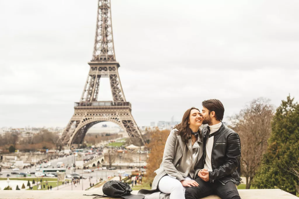 Young couple sitting on surrounding wall with a view on Eiffel tower.