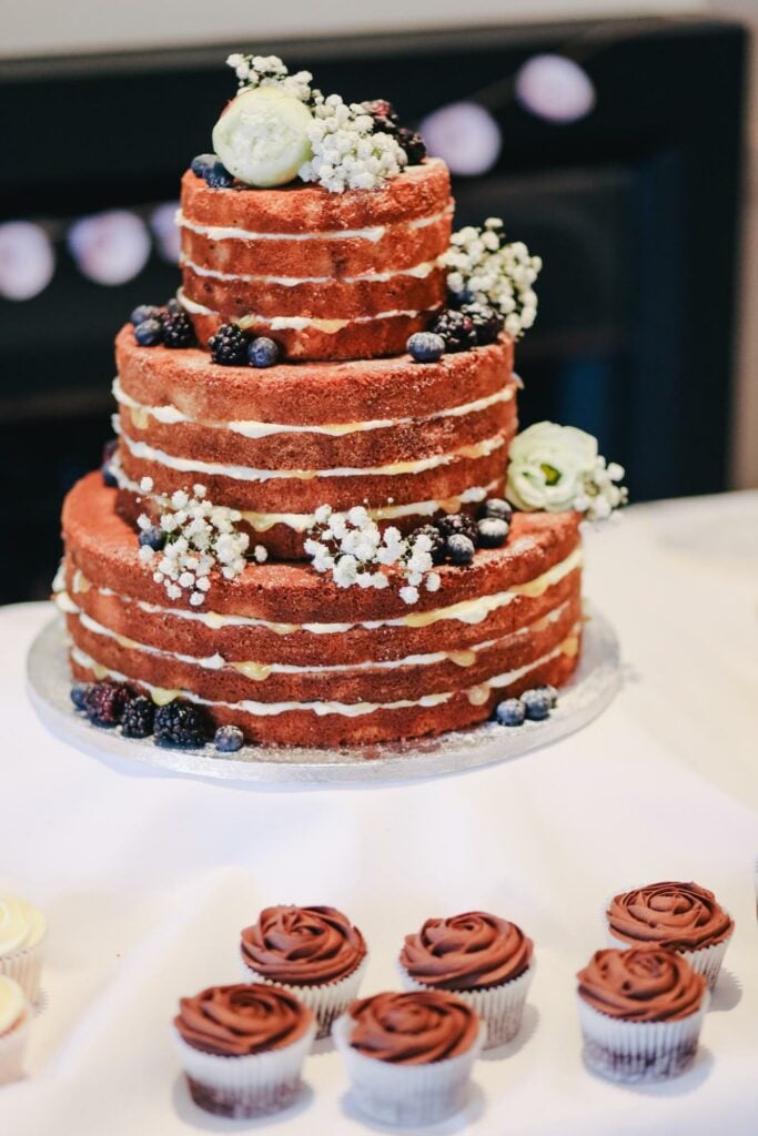 An extra naked wedding cake with little icing, berries, and flowers as decorations