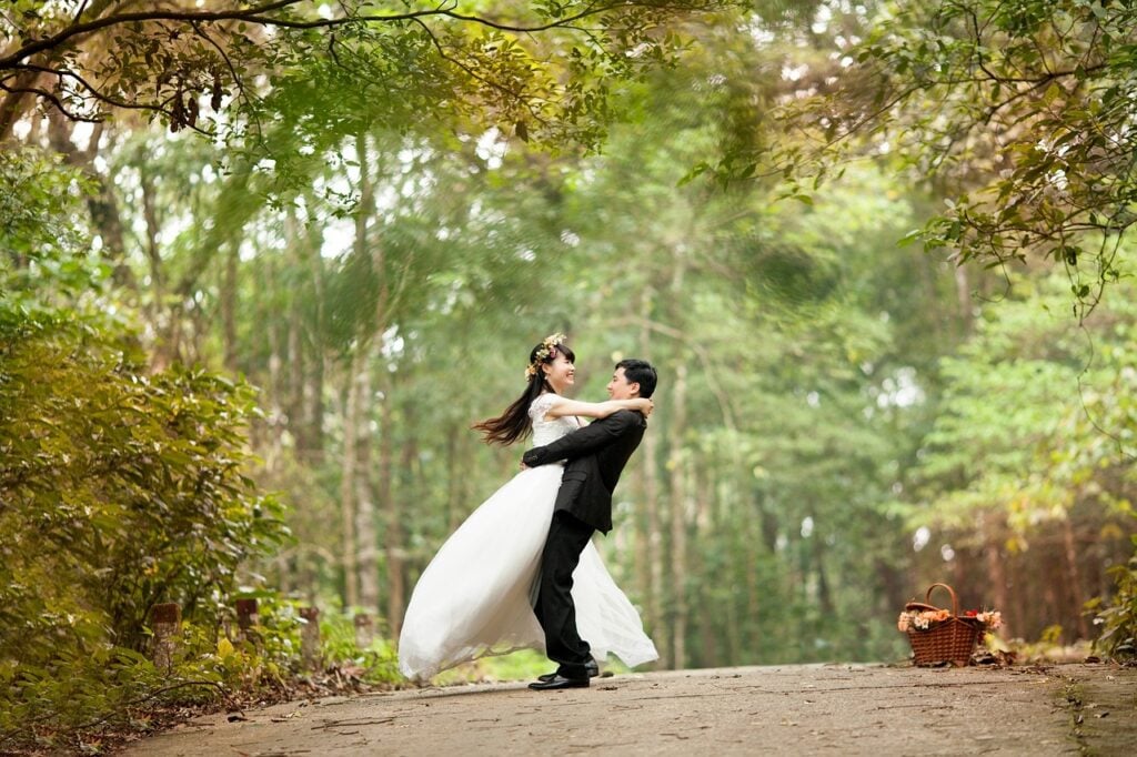 A couple poses for pictures on a road lined with trees at a private wedding venue