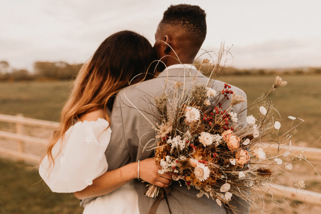 A newlywed couple embraces while looking at their wedding venue’s open field